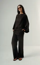 Camisa negra de manga ancha, estilo kimono o cruzado, con cierre frontal mediante botones de nudo.