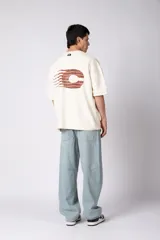 Remerón de corte oversized confeccionado en tejido rústico, con cuello redondo y mangas cortas. Presenta un diseño minimalista con una pequeña estampa frontal centrada en el pecho.