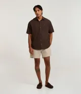 Camisa de corte relajado para hombre, confeccionada en una mezcla de cáñamo y algodón. Presenta cuello inglés, manga corta, cierre frontal con botones y un bolsillo en el pecho con una pequeña etiqueta aplicada.