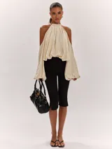 Top beige de diseño amplio y fluido, con cuello halter fruncido, hombros descubiertos y mangas largas abullonadas.