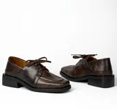 Zapato acordonado de cuero vacuno con acabado desgastado, de horma cuadrada y suela de goma con pequeño taco.