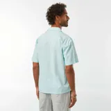 Camisa celeste de lino con cuello cubano, manga corta, cierre con botones y bolsillo en el pecho.