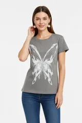 Remera gris de manga corta y cuello redondo al cuerpo, con gran estampado frontal abstracto de una mariposa y pequeños tachas metálicas en el escote y las mangas.