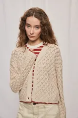 Cardigan de punto calado color beige, con escote en V, mangas largas y cierre frontal de botones. Presenta detalles de terminaciones en tono bordó.