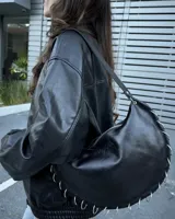 Cartera de hombro tipo hobo en color negro, confeccionada en cuero con acabado suave. Presenta un diseño de media luna con cierre superior y detalle de múltiples argollas metálicas plateadas dispuestas a lo largo del borde inferior y lateral. Incluye correa fija y el logo de la marca grabado discretamente en el frente.