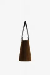 Bolso tipo tote amplio de ante marrón, con doble asa larga negra para el hombro y detalle gráfico frontal en forma de C con asas cortas integradas.