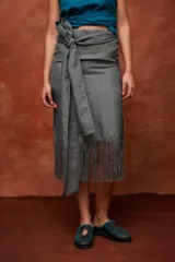 Falda midi color beige de tiro alto y silueta envolvente, con lazo ancho para anudar en la cintura, diseño asimétrico y terminación de flecos largos en el ruedo.