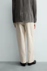 Pantalón chino de corte relajado, confeccionado en tejido estructurado de color beige. Presenta bolsillos frontales, bolsillos traseros de vivo y cierre frontal con cremallera y botón.