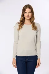 Buzo tejido en hilo de algodón color beige, con cuello redondo y manga larga. Presenta un corte clásico y un pequeño detalle metálico en la parte inferior izquierda.