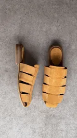 Zuecos de gamuza color tostado, con diseño de tiras cruzadas estilo romano y punta cuadrada.