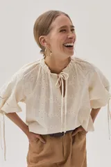 Blusa color crudo con bordado calado, cuello con volantes y lazos para ajustar. Mangas abullonadas con puños elásticos y lazos.