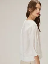 Blusa de algodón color marrón, con escote redondo, mangas tres cuartos con volumen sutil y costuras verticales decorativas en el frente.