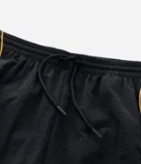 Pantalón deportivo de microfibra color negro, con corte holgado y diseño de piping contrastante en color amarillo. Cuenta con cintura elástica con cordón de ajuste, bolsillos laterales y logo bordado.