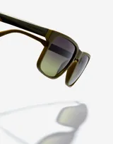 Gafas de sol Hawkers Peak Metal unisex, con montura cuadrada color verde oliva y lentes degradadas de negro a verde.