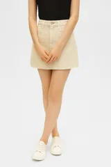Falda mini de jean color beige, con diseño de cinco bolsillos, cierre frontal con botón y ruedo deshilachado.