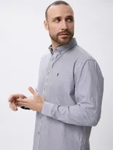 Camisa de manga larga con estampado de rayas verticales finas, cuello abotonado y cierre frontal con botones. Presenta un diseño clásico con detalle de logo bordado en el pecho.