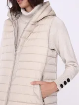 Chaleco largo color beige, matelaseado, con capucha y cierre frontal.