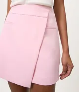 Short pollera de sastrería color rosado, con diseño asimétrico superpuesto en el frente, bolsillos ribeteados decorativos y cierre lateral discreto.