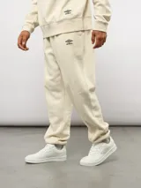 Pantalón de felpa color crema, con corte relajado, costuras verticales en la parte delantera y etiqueta con el logo de Umbro.
