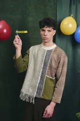 Buzo de manga larga con diseño patchwork que combina diferentes texturas y estampados, incluyendo tejido waffle verde oliva, tejido a rayas y cuadros en tonos grises y marrones, unidos con costuras visibles.