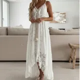 Vestido largo de encaje calado color blanco, con diseño de falda irregular más corta adelante. Presenta escote en V con cordones decorativos y borlas, tirantes finos y detalle de cintura marcada.