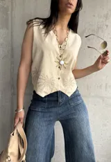 Chaleco color crema de lino liviano con bordado de palmeras en la terminación y corte recto.