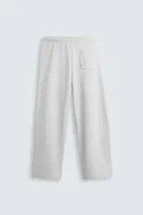 Pantalón jogger de corte relajado y pernera ancha, confeccionado en tejido de algodón con interior perchado. Cuenta con cintura elástica ajustable mediante cordón interior, bolsillos laterales y un bolsillo trasero de plastrón.