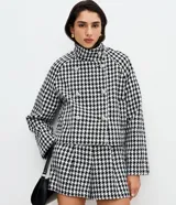 Saco corto estructurado con estampado pied de poule en blanco y negro. Presenta cuello alto, cierre frontal cruzado con botones decorativos y mangas largas.