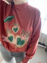 Buzo cropped de algodón color rojo con estampa frontal exclusiva de corazones con diseño de cerezas y hojas, manga larga y cintura elastizada.