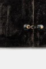Chaleco de efecto pelo con capucha, manga sisa y cierre frontal mediante alamares metálicos. Cuenta con bolsillos laterales de vivo y forro interior a tono.