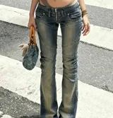 Jean de tiro bajo con efecto desgastado y costuras decorativas que realzan la silueta. Presenta un corte ajustado en la cadera y muslos con una leve apertura acampanada en la botamanga, incorporando un cierre frontal visible.