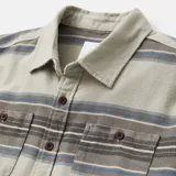 Camisa de franela a rayas horizontales en tonos beige, gris, azul y blanco, con cuello clásico, manga larga, dos bolsillos con botón en el pecho y cierre frontal con botones marrones.