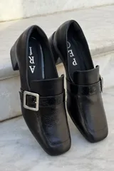 Mocasín de cuero vacuno color bordó con acabado charolado, punta cuadrada, taco bloque bajo y detalle de tira con hebilla metálica plateada en el empeine.