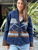 Campera de punto azul marino, con cuello smoking acanalado, bolsillos frontales aplicados y cierre de botones. Presenta bandas horizontales grises y marrones, y detalles geométricos en el frente.