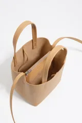 Bolso pequeño de piel vacuna color negro, con estructura rígida, doble asa de mano y correa larga ajustable para llevar al hombro o cruzado. Presenta cierre de botón a presión y logo metálico de la marca en el frente.