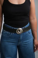 Cinto trenzado de cuero negro con hebilla circular metálica grabada y detalle central de piedra natural.