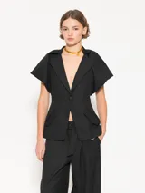 Blazer negro de lanita viscosa con cuello mao y mangas ranglan abullonadas tipo balloon con frunces en la unión con el cuello. Incluye pinza lateral que mejora el calce en la sisa, bolsillos ojal con tapa y cierre con broche bombé super black.