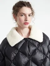 Chaqueta negra capitoneada con diseño de rombos, cuello de corderito blanco y paneles laterales de corderito a tono. Presenta cierre frontal con botones a presión.