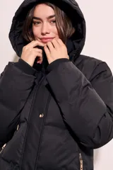 Tapado negro largo con capucha, diseño capitoneado y cierre frontal con botones dorados.