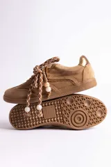 Zapatillas urbanas de gamuza color marrón, con diseño de cordones decorados con cuentas de piedra y detalles de líneas brillantes en los laterales. Presentan suela de goma texturizada al tono.