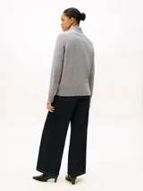 Sweater gris de corte regular y manga raglán, confeccionado en pura lana. Presenta cuello perkins, puños y bajo en punto canalé, y un escudo gráfico distintivo de la marca tejido en el pecho.