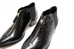 Botin de cuero negro con acabado charol y textura de reptil. Presenta cierre frontal con cremallera, paneles laterales elásticos y tacón bajo de bloque.