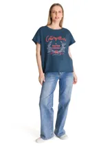 Remera de corte relajado color azul, con cuello redondo y mangas cortas con dobladillo. Presenta un estampado gráfico frontal con la inscripción Caterpillar A Tractor Company en tonos rojos y detalles botánicos.