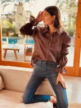 Camisa marrón de algodón con cuello clásico, cierre frontal con botones dorados y mangas largas abullonadas con puños elásticos.