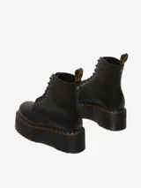 Botas Dr. Martens modelo 1460 Pascal Max de cuero negro, con plataforma gruesa acanalada, cordones negros, ojales metálicos plateados y costuras amarillas distintivas. Incluye tirador trasero con logo en amarillo y negro.