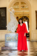 Vestido largo color rojo, de corte holgado con escote en V y mangas largas acampanadas. Presenta un detalle de volado horizontal en la cintura que aporta volumen y movimiento a la prenda.