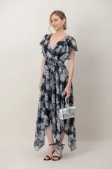 Vestido midi de gasa estampada con flores en tonos negro, gris y blanco, con destellos de hilos de plata. Presenta escote cruzado en V, mangas cortas acampanadas, lazo ajustable en la cintura y falda de corte asimétrico.