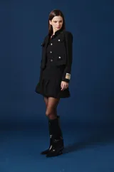 Saco corto color bordó con cuello mao, cierre frontal de botones dorados y cuatro bolsillos delanteros con solapa y botón dorado. Presenta un parche decorativo en la manga izquierda.