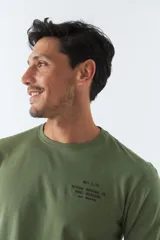 Remera verde militar de manga larga, cuello redondo y corte recto. Estampa pequeña en el pecho con texto en negro.