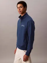 Buzo Calvin Klein de color azul marino, confeccionado en mezcla de algodón y poliéster. Cuenta con cuello alto, cierre de media cremallera y manga larga con hombros caídos. Presenta puños y dobladillo acanalados, y el logo de la marca bordado en punto de cadeneta en el pecho.